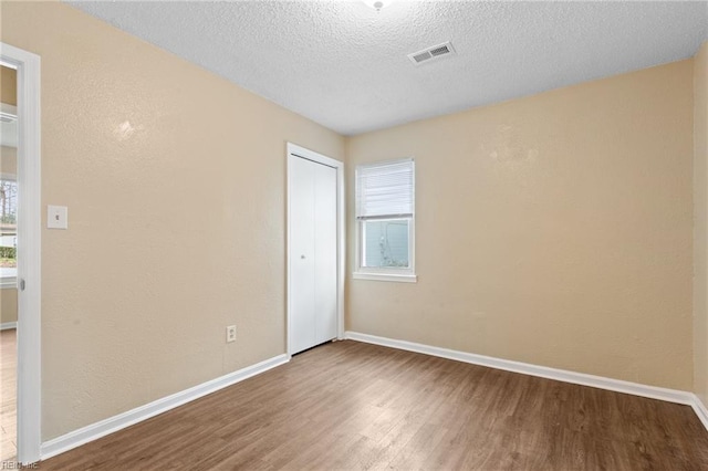 unfurnished room featuring baseboards, a textured ceiling, visible vents, and wood finished floors