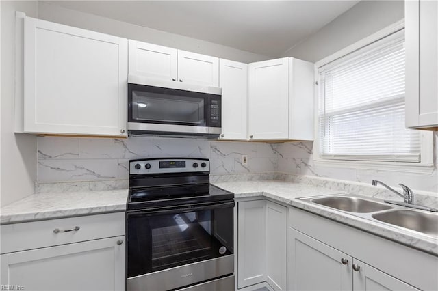 kitchen with white cabinets, a sink, stainless steel appliances, light countertops, and backsplash