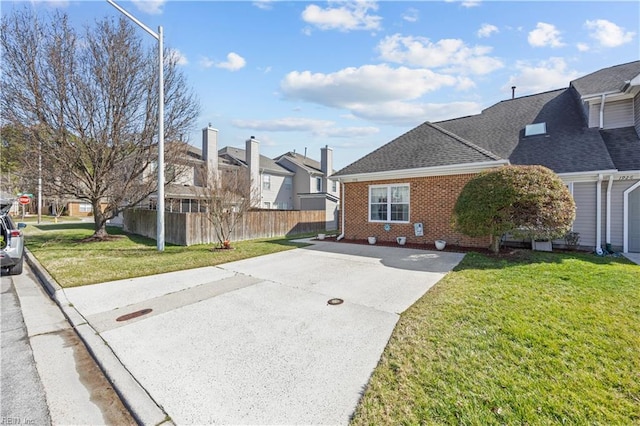 view of home's exterior with a yard, brick siding, roof with shingles, and fence