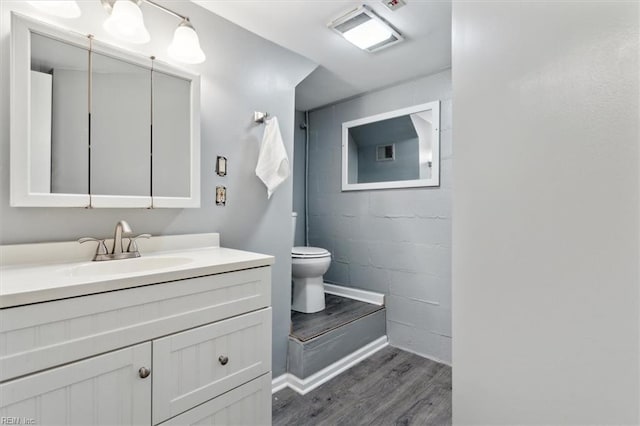 bathroom featuring toilet, wood finished floors, vanity, visible vents, and concrete block wall