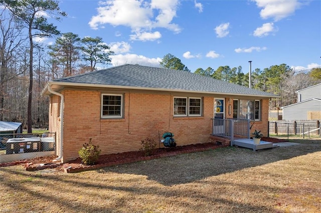 rear view of house featuring brick siding, a lawn, and fence