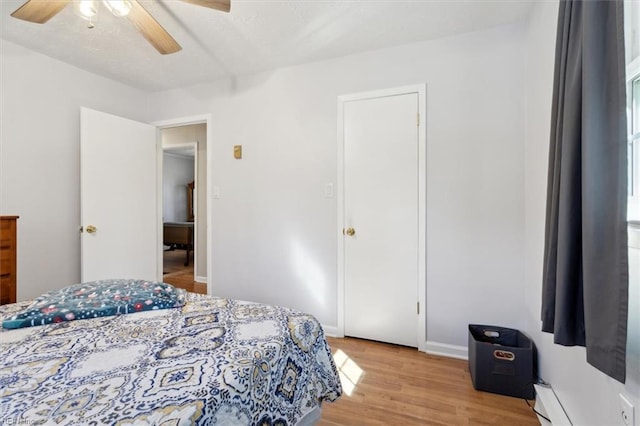 bedroom with light wood-style floors, baseboards, a baseboard heating unit, and ceiling fan