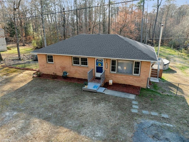 view of front of house featuring a forest view, brick siding, a shingled roof, and fence