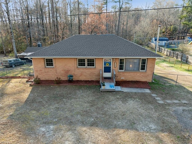 view of front of property featuring a shingled roof, entry steps, brick siding, and fence