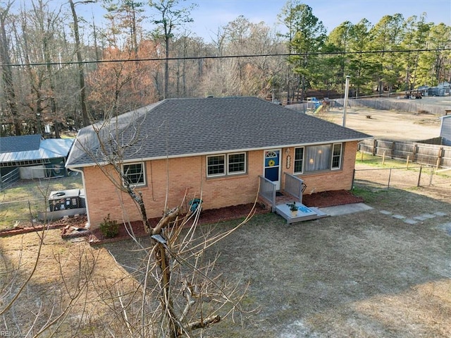 view of front facade featuring brick siding, fence, and roof with shingles
