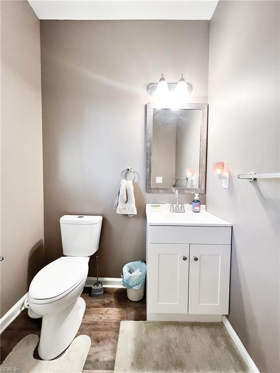 half bathroom with toilet, baseboards, wood finished floors, and vanity