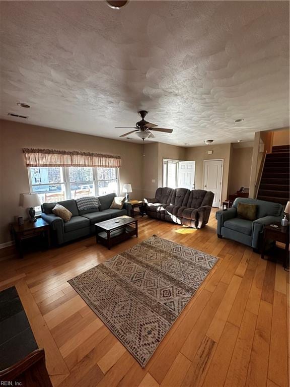 living room with visible vents, a ceiling fan, light wood-style flooring, stairs, and a textured ceiling