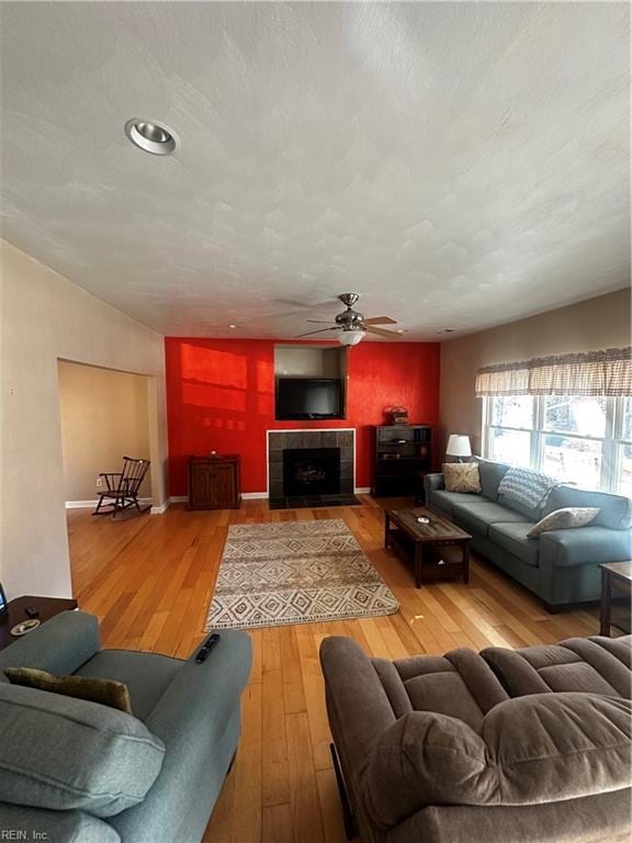 living area featuring hardwood / wood-style flooring, a textured ceiling, a ceiling fan, and a tile fireplace