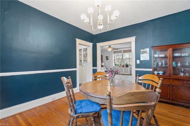 dining space with baseboards, wood finished floors, and ceiling fan with notable chandelier