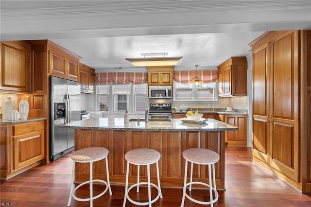 kitchen with dark wood-style flooring, brown cabinets, stainless steel appliances, a wealth of natural light, and an island with sink