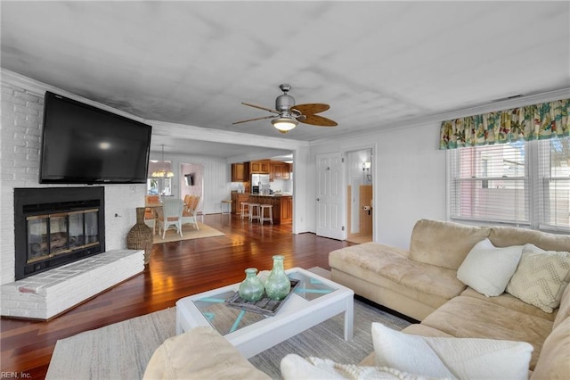 living area featuring dark wood-style floors, a brick fireplace, crown molding, and ceiling fan