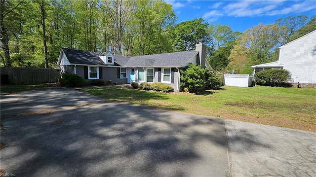 view of front of home with aphalt driveway, fence, a chimney, and a front lawn