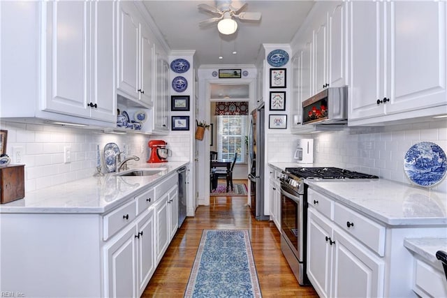 kitchen featuring white cabinets, appliances with stainless steel finishes, ornamental molding, wood finished floors, and a sink