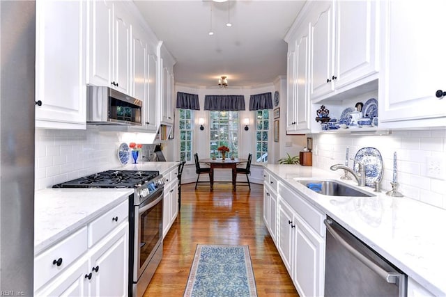 kitchen with appliances with stainless steel finishes, light wood-type flooring, a sink, and white cabinetry