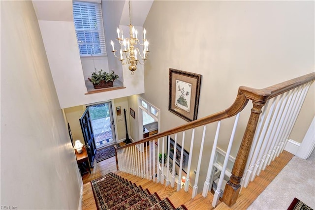 stairs featuring a chandelier, a towering ceiling, baseboards, and wood finished floors