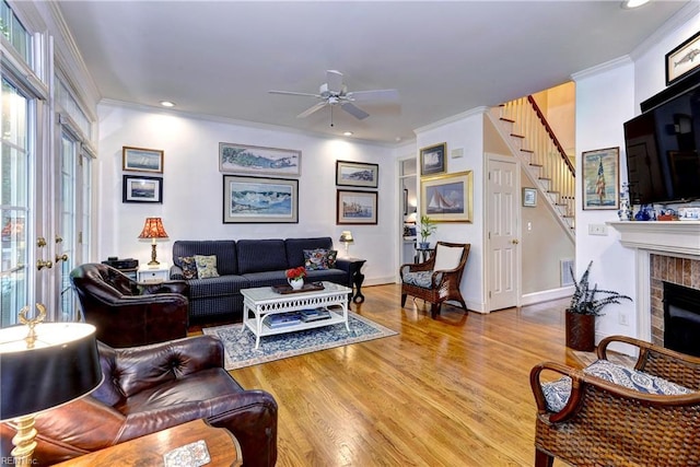 living area with ornamental molding, a brick fireplace, wood finished floors, baseboards, and stairs