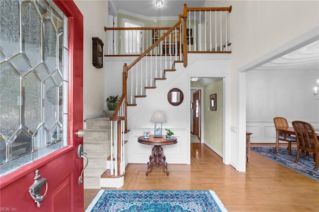 foyer with a decorative wall, a high ceiling, ornamental molding, wood finished floors, and stairs