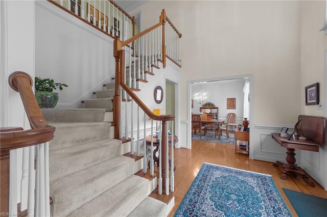 stairs with a wainscoted wall, a high ceiling, and wood finished floors