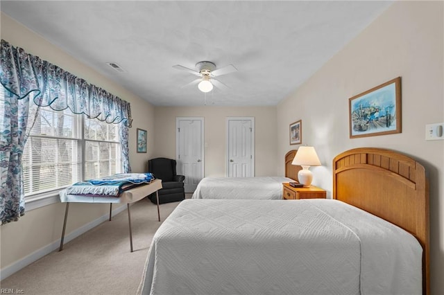 bedroom with light carpet, visible vents, a ceiling fan, baseboards, and two closets