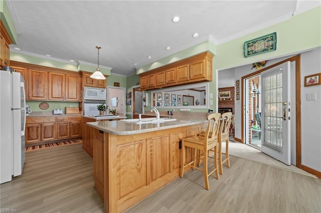 kitchen featuring light wood finished floors, white appliances, a sink, and brown cabinets