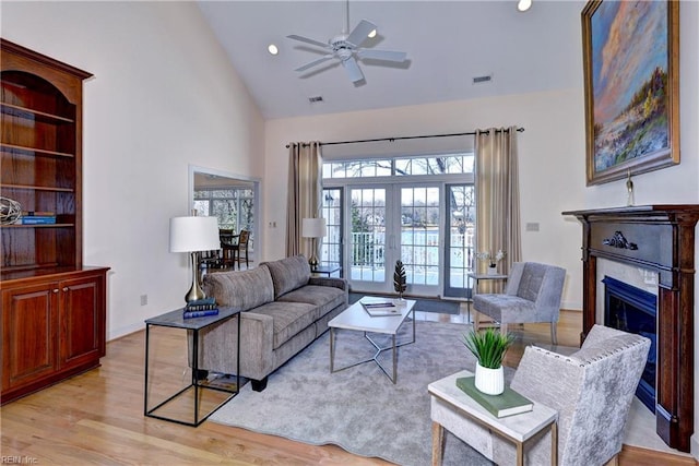 living area featuring high vaulted ceiling, a fireplace, visible vents, light wood-style floors, and french doors