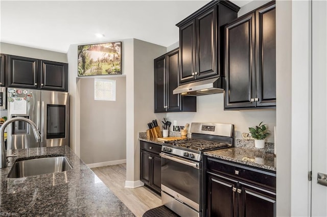 kitchen with stainless steel appliances, a sink, under cabinet range hood, and dark stone countertops