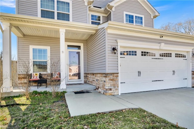 entrance to property with stone siding, covered porch, concrete driveway, and a garage