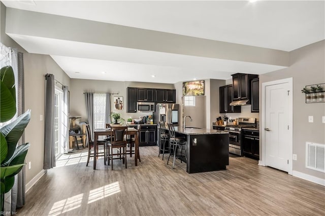 kitchen featuring a breakfast bar, visible vents, appliances with stainless steel finishes, light wood-style floors, and a sink