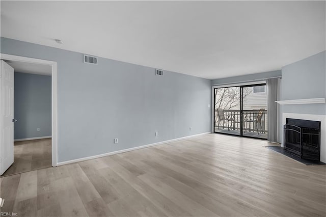 unfurnished living room with baseboards, a fireplace, visible vents, and light wood-style floors