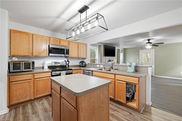 kitchen with a peninsula, light wood-type flooring, stainless steel appliances, and a sink