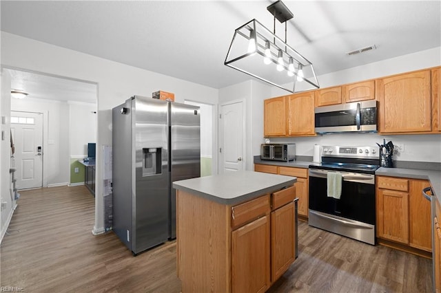 kitchen with visible vents, dark wood finished floors, a kitchen island, stainless steel appliances, and pendant lighting