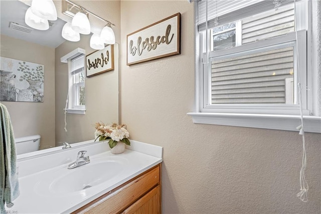 bathroom featuring toilet, a textured wall, visible vents, and vanity