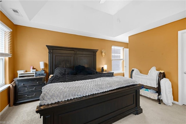 bedroom featuring a tray ceiling, multiple windows, visible vents, and light colored carpet