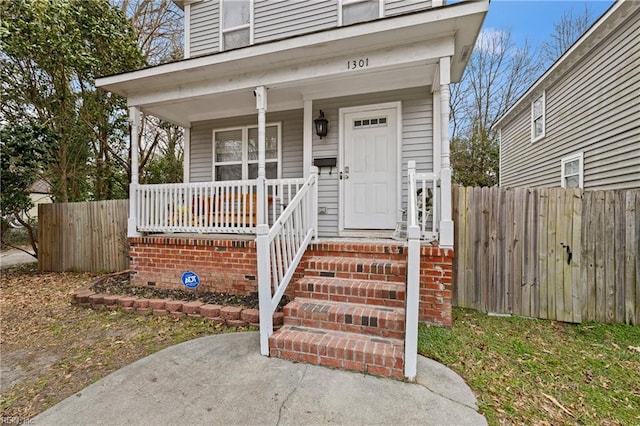 doorway to property with a porch and fence