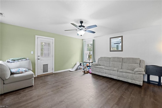 living room featuring dark wood-type flooring, visible vents, baseboards, and a ceiling fan