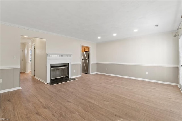 unfurnished living room with crown molding, recessed lighting, light wood-style floors, a glass covered fireplace, and wainscoting