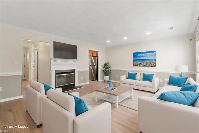 living area featuring ornamental molding, a glass covered fireplace, light wood finished floors, and recessed lighting