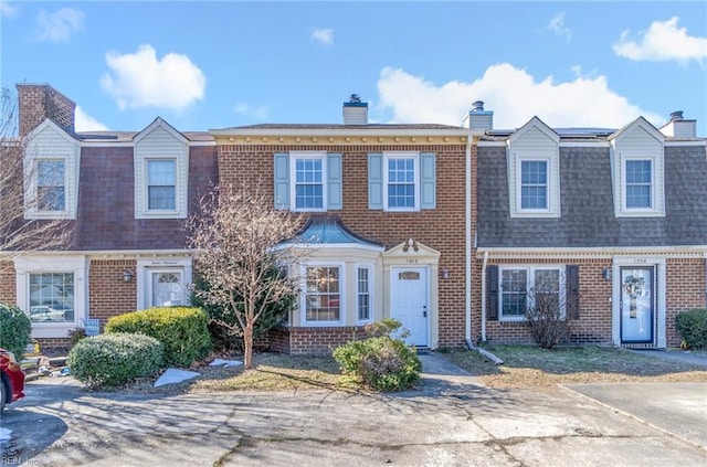 multi unit property featuring a shingled roof, a chimney, and brick siding