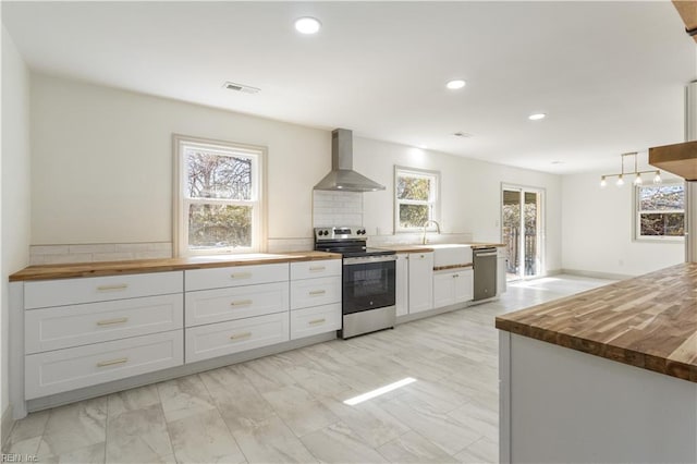 kitchen with butcher block counters, visible vents, appliances with stainless steel finishes, white cabinetry, and wall chimney range hood