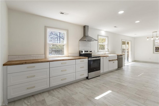 kitchen with stainless steel appliances, butcher block counters, white cabinetry, a sink, and wall chimney exhaust hood