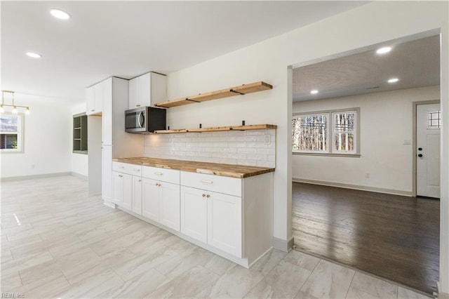 kitchen with open shelves, stainless steel microwave, backsplash, white cabinets, and wood counters