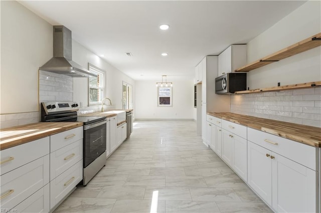 kitchen featuring marble finish floor, stainless steel appliances, wall chimney exhaust hood, and white cabinets