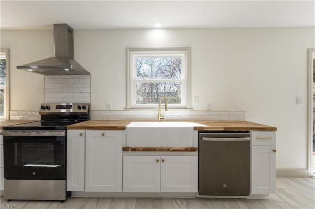 kitchen featuring white cabinets, wall chimney exhaust hood, wood counters, stainless steel appliances, and a sink