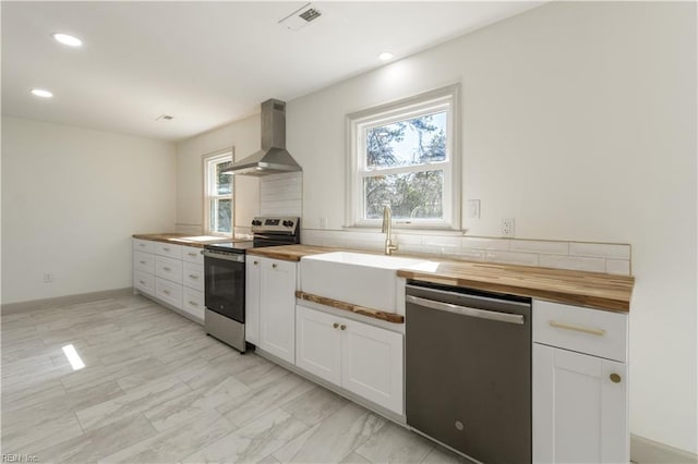 kitchen with stainless steel appliances, visible vents, white cabinetry, wood counters, and wall chimney range hood