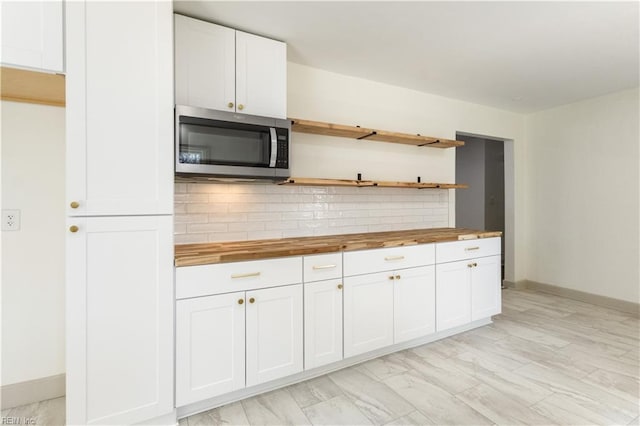 kitchen with tasteful backsplash, stainless steel microwave, white cabinetry, open shelves, and wooden counters