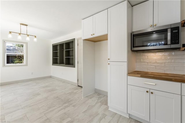 kitchen featuring butcher block countertops, white cabinetry, decorative backsplash, stainless steel microwave, and decorative light fixtures