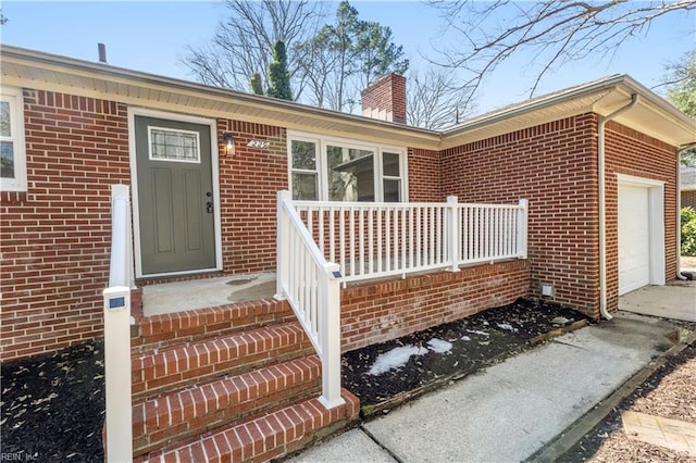 entrance to property featuring a garage, brick siding, and a chimney