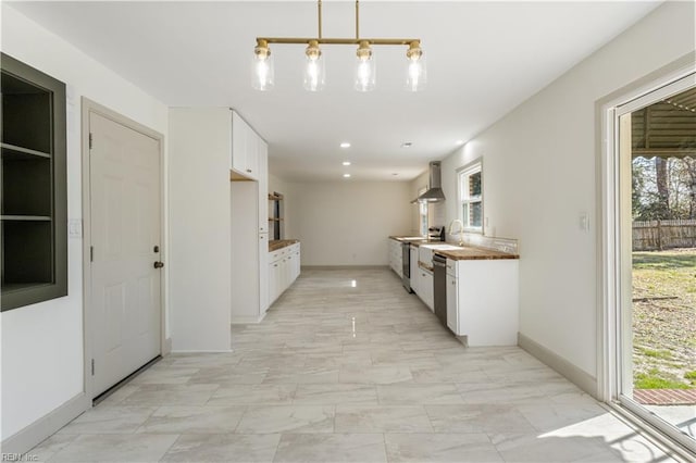 kitchen with marble finish floor, hanging light fixtures, stove, white cabinets, and wall chimney exhaust hood