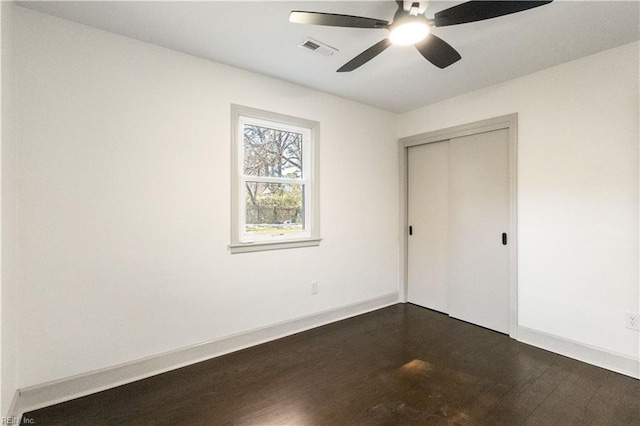 unfurnished bedroom featuring a closet, visible vents, dark wood-type flooring, ceiling fan, and baseboards