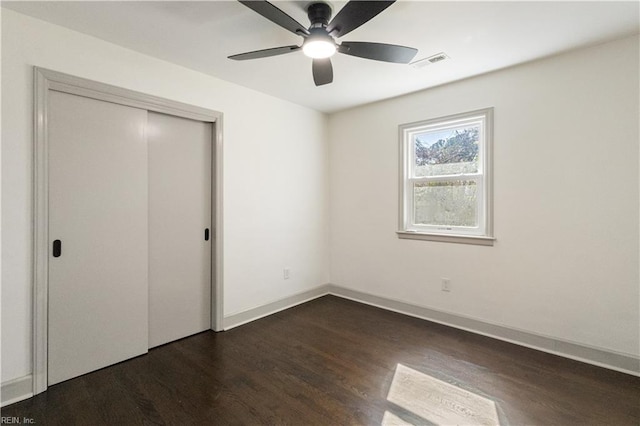 unfurnished bedroom featuring dark wood finished floors, a closet, visible vents, ceiling fan, and baseboards